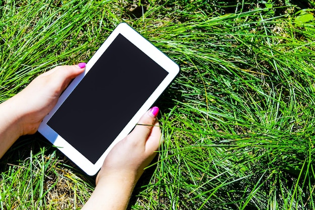 Woman's hands holding white tablet with blank skreen on green gr