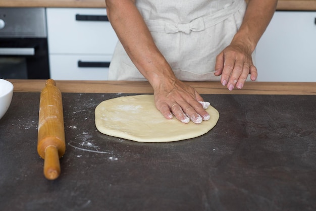 A woman's hands roll out the dough on a dark table Preparation of the dough