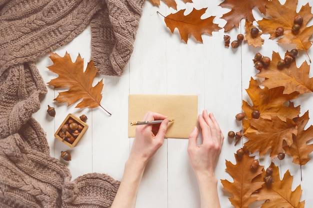 Woman's hands sign an envelope with a greeting card Top view Autumn time concept