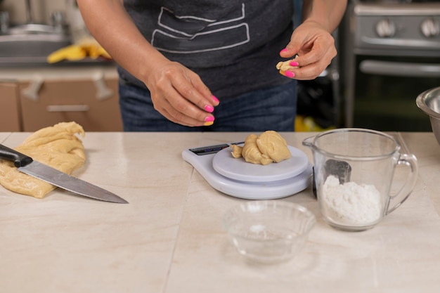 Woman's hands weighing portions of dough to make pan de muerto at her kitchen counter