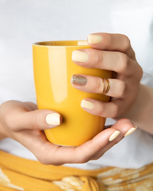 Woman's hands with yellow shiny nail design holding cup.