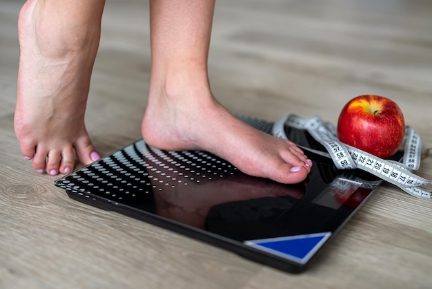 Woman's legs standing on scales and a tape measure and an apple nearby in the middle hall