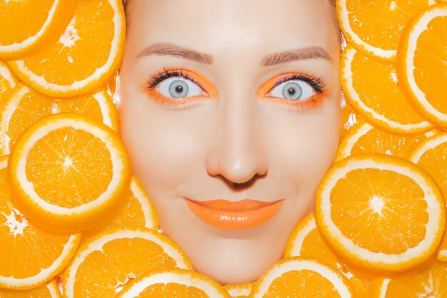 Woman's portrait with oranges closeup. Bright orange make up