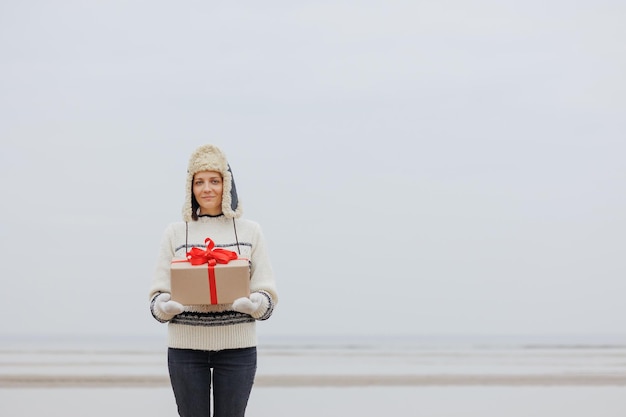 Woman in a Santa Claus hat with a gift box in her hands smiles a happy European woman carries a gift for New Year or Christmas