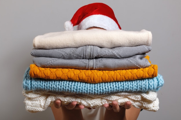 Woman in santa hat holding a stack of warm knitted sweaters