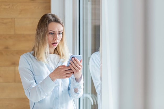 woman saw bad news on smartphone standing by the window in the office or at home