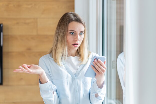 woman saw bad news on smartphone standing by the window in the office or at home