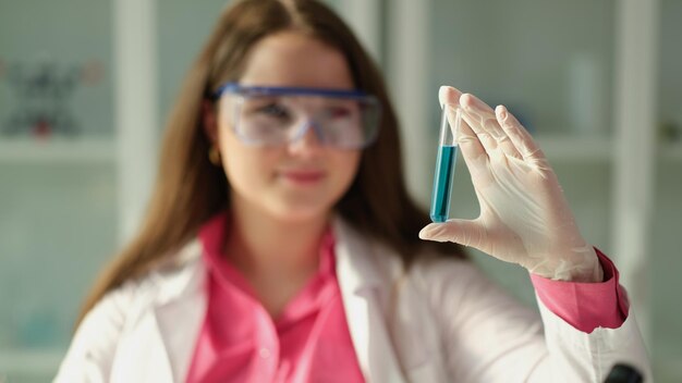 Woman scientist chemist holding test tube with blue liquid in chemical laboratory closeup