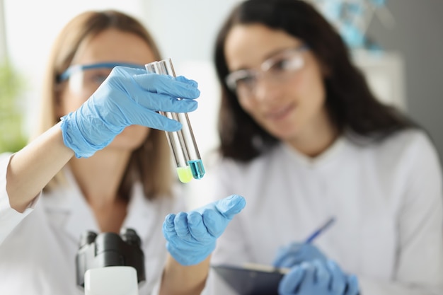 Woman scientist chemist showing test tubes with blue and yellow liquid in laboratory closeup