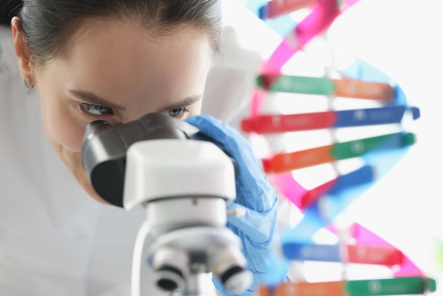 Woman scientist looking through microscope near dna molecule mockup in lab