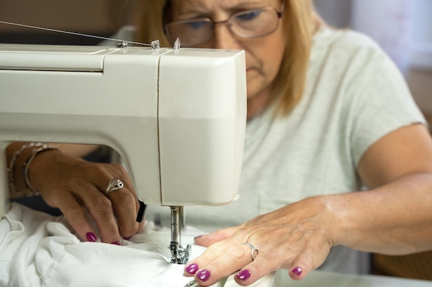 Woman seamstress with glasses concentrating while sewing at the sewing machine