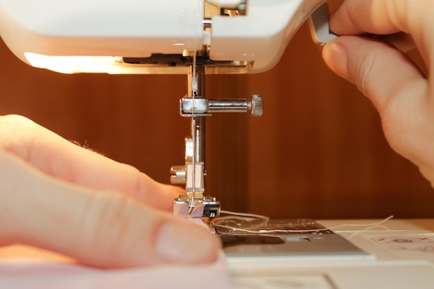 A woman sews on a white electric sewing machine. The concept of sewing, cutting, needlework.