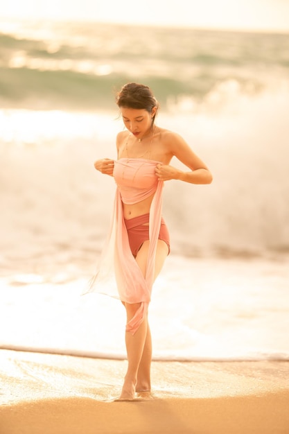 Woman in sexy swimwear posing on the tropical beach in sunset light