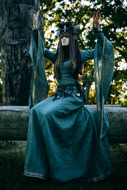 Woman-shaman with horns in green dress walk in forest