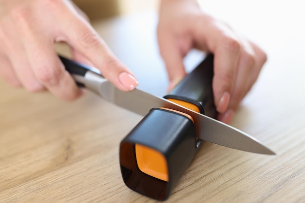 Photo woman sharpens knife with sharpener in kitchen closeup