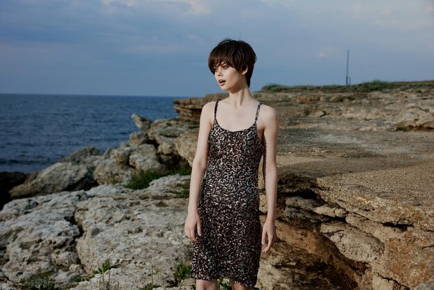 Woman in a shiny dress stands on the stone coast of the ocean nature