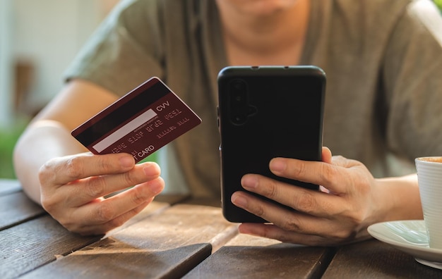 Woman shopping online with credit card at coffee shop in outdoorclose up hand holding smartphone