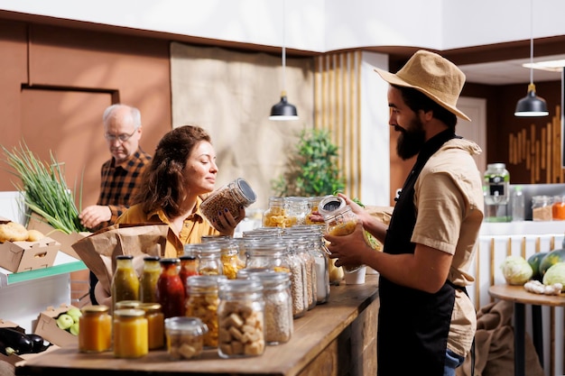 Woman shopping in zero waste grocery store, looking at bulk products in reusable packaging while being assisted by helpful clerk. Customer in local neighborhood picking ethically produced food