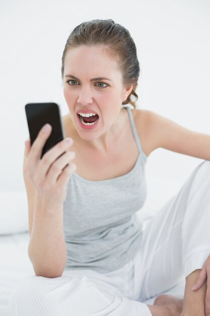 Woman shouting into mobile phone in bed