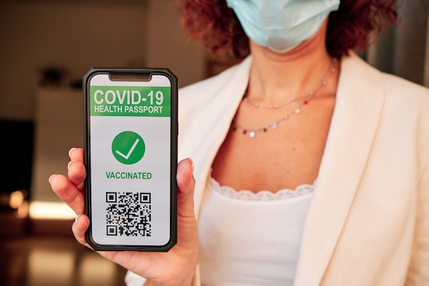 Woman showing covid-19 health passport on smartphone with qr code to get access