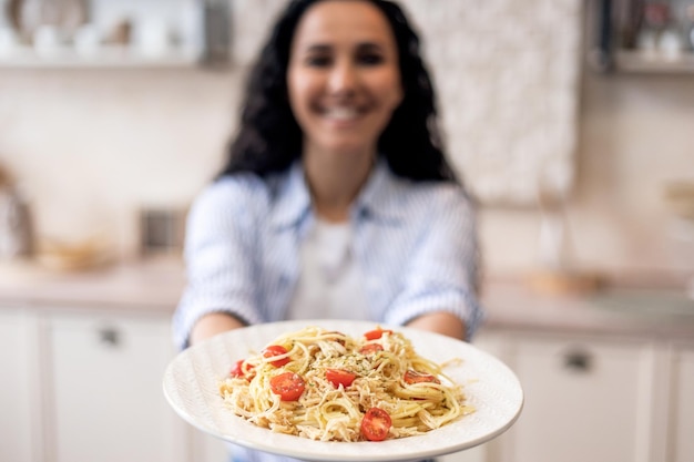 Woman showing homemade pasta in the dish stretching meal to camera and smiling focus on plate with