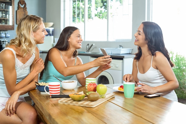 Woman showing mobile phone to friend at breakfast table