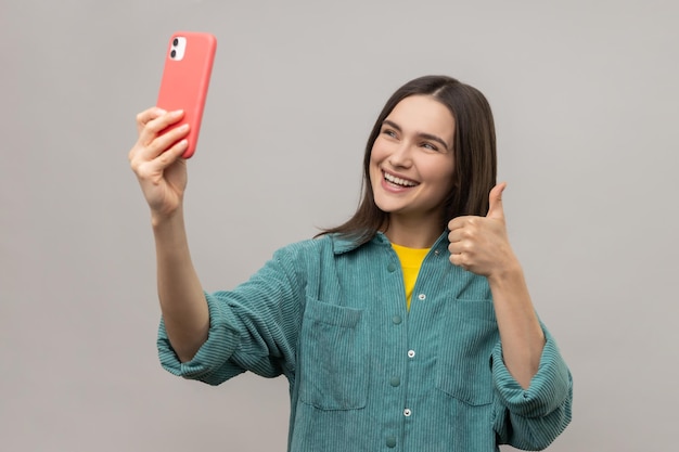 Woman showing thumb up while communicating by video call or streaming taking selfie on smartphone