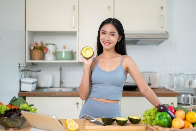 A woman shows an avocado to the camera while she prepares her healthy meals in the kitchen