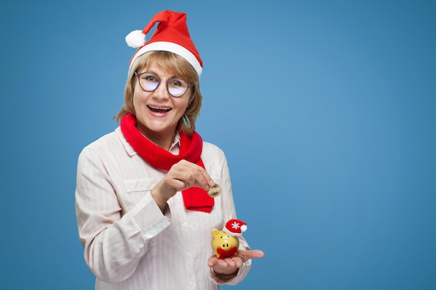 The woman shows the pig piggy Bank A middleaged woman in the new year and Christmas clothes on a blue background