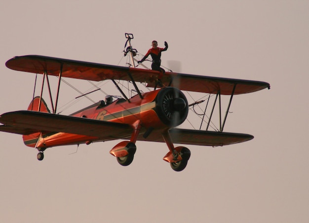 A woman shows tricks on the wing of a retro airplane in the sky