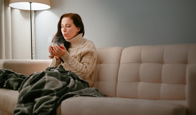 Woman sick with flu with a cup of hot cough tea blowing on him