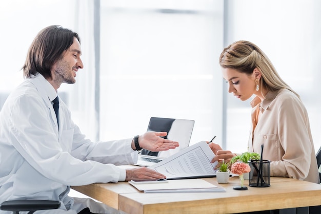 Woman signing insurance claim form during appointment with doctor in clinic