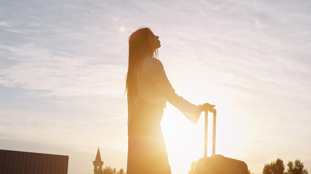 Woman silhouette stands with suitcase at back cloudy sunset