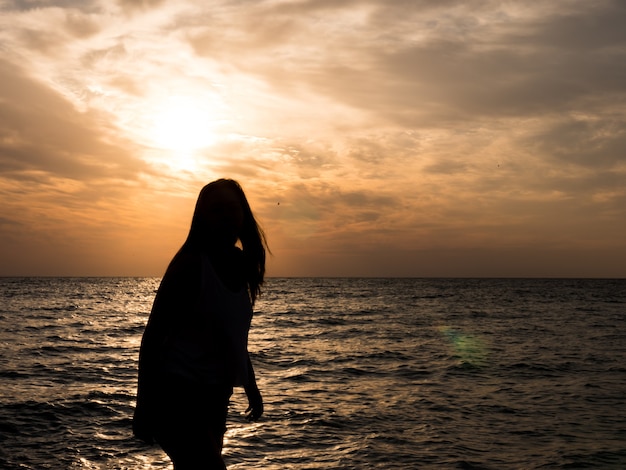 Woman silhouette watching sun on the beach at sunset.. Tourist girl on beach holiday