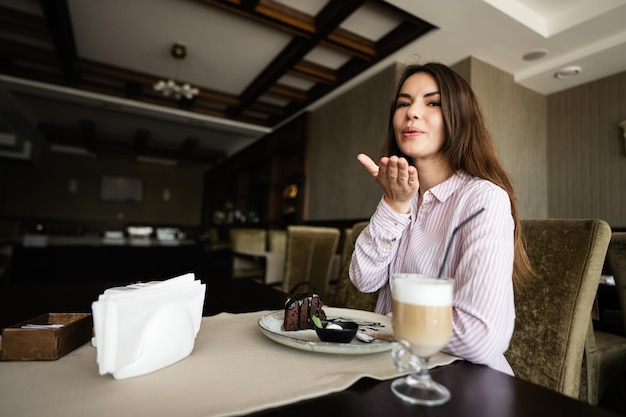 woman sit in coffee shop cafe restaurant indoors and send air kiss to camera