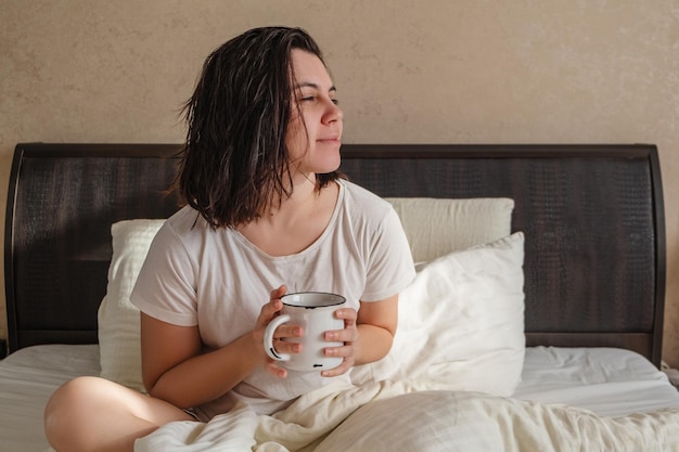 A woman sits in bed with a mug of coffee.