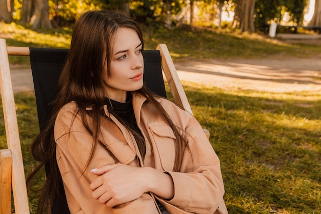 A woman sits in a chair in a park looking away from the camera