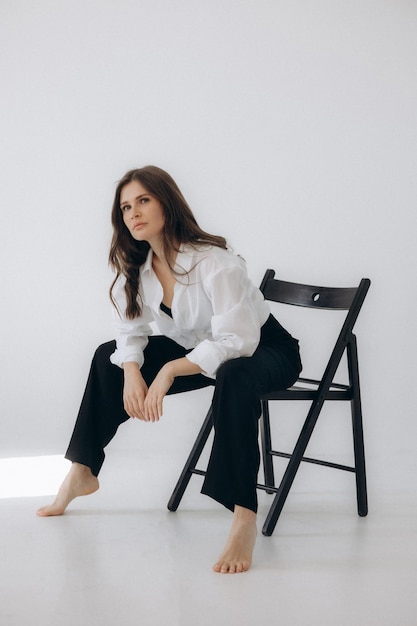 A woman sits on a chair in a white room