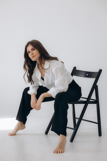 A woman sits on a chair in a white room