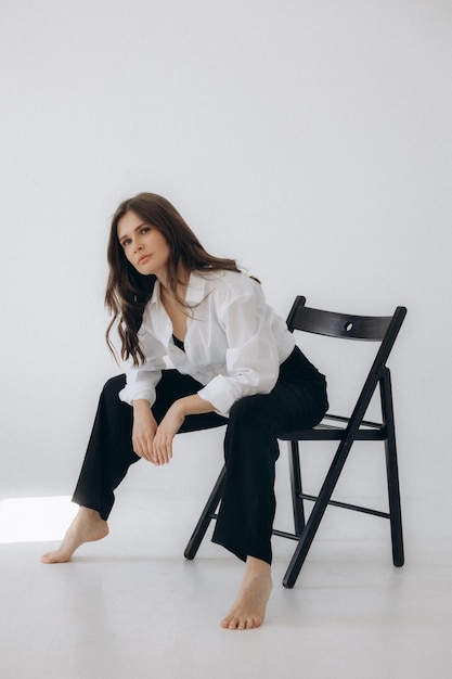 A woman sits on a chair in a white room.