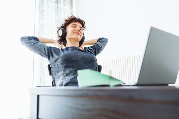 A woman sits at a desk with headphones on and a laptop in front of her.