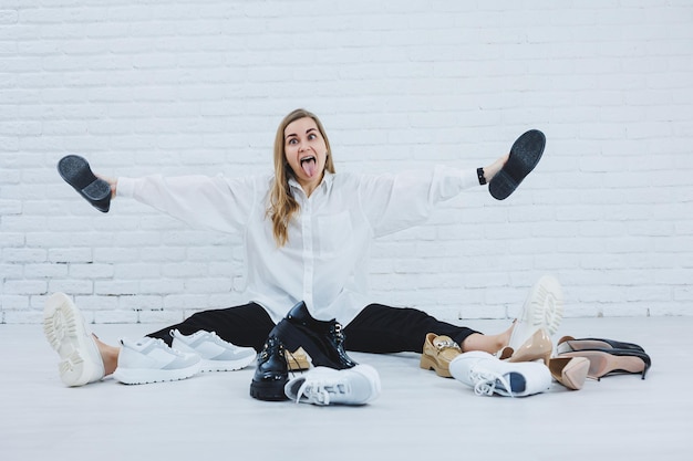 A woman sits on the floor in a dressing room between shoes and chooses new shoes for herself Lady in a white shirt Woman in white shoes