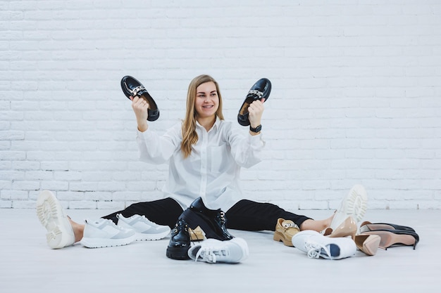 A woman sits on the floor in a dressing room between shoes and chooses new shoes for herself Lady in a white shirt Woman in white shoes