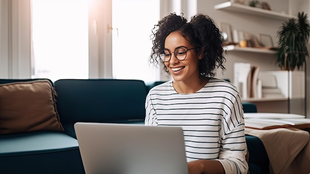 A woman sits in front of a couch and smiles at a laptop.