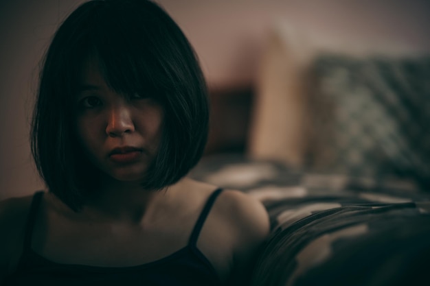 A woman sits next to her bed and looks at the camera with a gloomy and frightening expression