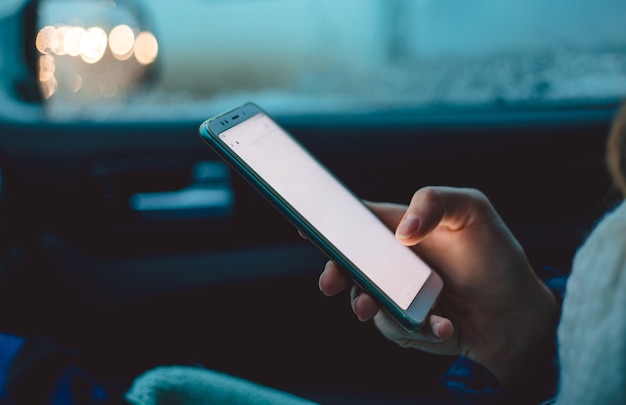 A woman sits in the passenger seat of a car and uses a smartphone in the early winter morning.