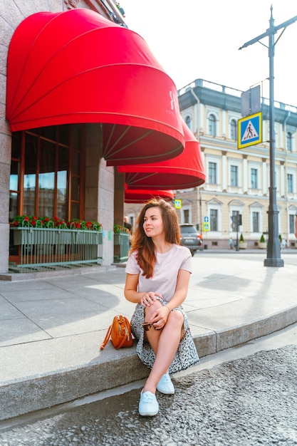 a woman sits on the sidewalk under the red awning in st petersburg on a sunny day