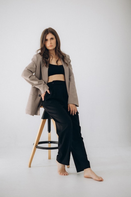 A woman sits on a stool wearing a blazer and black pants.