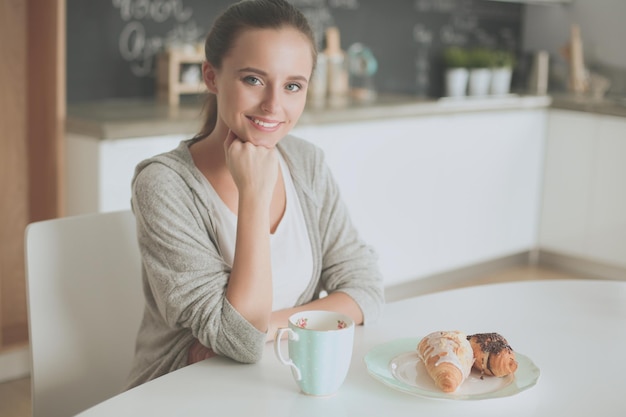 A woman sits at a table with a plate of food and a croissant.