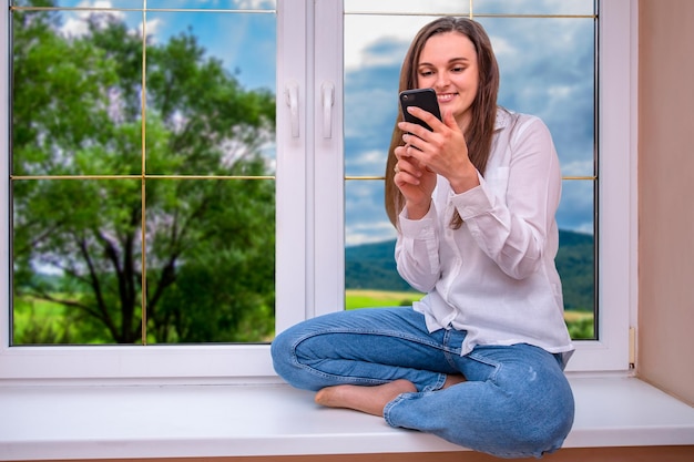 A woman sits on a windowsill and looks at her phone.